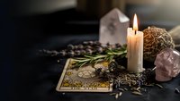 Mystical tarot card reading setup with burning candle, crystals, herbs and spiritual elements on dark surface for divination and fortune telling practices.
