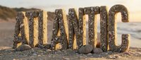 Sand and shell letters spelling Atlantic on a sunny beach with ocean backdrop, evoking coastal summer vibes for travel and decor.