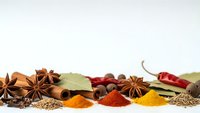 Colorful spices and herbs arranged on white background with star anise, bay leaves, chili peppers, turmeric, paprika creating culinary ingredient display.