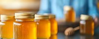 Fresh golden honey in glass jars arranged on wooden surface with honey dipper, natural sweetener and organic food product in warm ambient lighting.