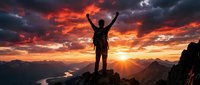 Silhouette of triumphant hiker with raised arms celebrating success on mountain peak at dramatic sunset with orange and red clouds over valley landscape.
