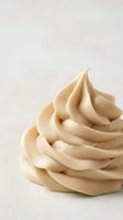 Swirled vanilla or caramel frosting piped in soft peaks on white background, isolated and ready for bakery, dessert, and confectionery design projects.