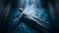 Young man floating in mystical blue smoke with arms outstretched in dark atmospheric setting for supernatural and fantasy concepts.