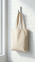 Blank beige cotton tote bag hanging on chrome hook against white brick wall background for eco-friendly shopping and sustainable lifestyle mockup.