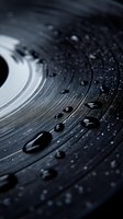 Water drops on black vinyl record surface creating artistic macro photography effect. Dark moody atmosphere with selective focus on grooves and droplets.