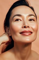 Young Asian woman with glowing skin and red lipstick smiling confidently against peach background, showcasing natural beauty and radiant complexion for cosmetic advertising.