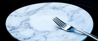 Empty marble plate with fork on black background, minimalist dining and restaurant design concept.