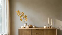 Autumn home decor with golden branches in vase, white pumpkins and candles on wooden sideboard against beige wall creating cozy seasonal interior design.