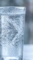 Clear glass filled with sparkling carbonated water showing effervescent bubbles rising to surface with condensation droplets on exterior for refreshment concepts.