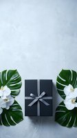 Elegant black gift box with gray ribbon surrounded by tropical monstera leaves and white orchid flowers on textured concrete background for luxury occasions.