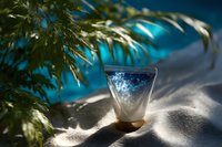 Refreshing blue and white layered drink in glass with tropical palm leaf shadow on sand background creates summer beach atmosphere and mood.