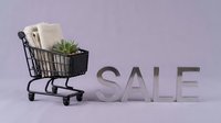 Mini shopping cart with towels and succulent plant beside metallic SALE letters on soft purple background, retail discount concept.