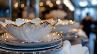 Elegant white porcelain plates with gold trim stacked on table with soft bokeh lights in background, creating luxurious dining atmosphere for events and celebrations.