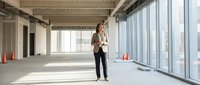 Woman in business casual attire standing in empty modern office space with floor-to-ceiling windows, suitable for corporate, real estate, and startup concepts.