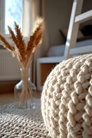 Cozy knitted pouf and dried pampas grass in glass vase create serene boho interior atmosphere with natural textures and warm neutral colors.