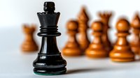 Black chess queen piece in focus with blurred wooden pawns in background, symbolizing leadership and strategic advantage in gameplay.