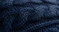 Navy blue cable knit wool sweater texture with intricate braided pattern detail for cozy winter fashion and textile design projects.