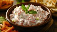 Fresh salmon dip with diced vegetables and herbs in rustic ceramic bowl, served with raw carrot sticks and crackers, garnished with mint leaf.