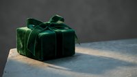 Elegant emerald green velvet gift box with satin ribbon bow on dark surface for luxury holiday celebrations and special occasions.
