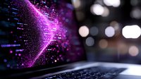 Glowing purple digital particles form dynamic wave pattern over laptop keyboard with bokeh background, representing data visualization and technology concept.