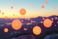 Glowing orange paper lanterns floating against mountain sunset skyline create magical atmosphere at outdoor celebration or festival gathering.