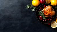Roasted chicken with fresh cranberries, rosemary sprigs, and citrus fruits arranged on dark background with copy space. Food photography for restaurant menu.