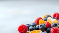 Fresh mixed berries including blueberries, raspberries and orange slices arranged on white background with copy space for healthy eating concepts.
