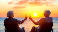 Elderly couple toasting champagne glasses while watching orange sunset over ocean from beach chairs, romantic vacation moment for senior travelers.