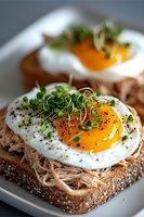 Gourmet open sandwich with pulled chicken, sunny side up egg, microgreens and black pepper on seeded bread. Bright orange yolk and fresh garnish create appetizing breakfast.