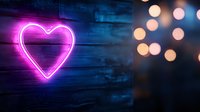 Glowing pink neon heart sign on dark wooden wall with blurred bokeh lights creating romantic atmosphere, suitable for Valentine's Day or love themes.