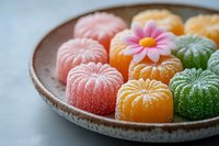 Colorful fruit jellies shaped like flowers arranged on ceramic plate. Sweet confectionery treats in pink, orange and green colors dusted with sugar crystals.