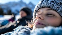 Young woman with freckles relaxing in fresh snow wearing winter knit hat, eyes closed with peaceful expression against snowy mountain backdrop.