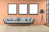 Modern living room interior with gray sofa, three empty black frames on coral pink wall, wooden floor and tripod floor lamp near window.