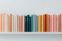Row of books arranged by color on white shelf creating rainbow gradient effect from peach through teal, gold, and pink spines, minimal contemporary style.