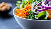 Fresh colorful salad bowl with sliced carrots, red onion rings, green leafy vegetables and black sesame seeds on blue background, healthy eating concept.