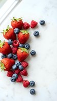 Fresh mixed berries strawberries blueberries raspberries scattered on white marble surface with natural sunlight for healthy eating and nutrition concepts.