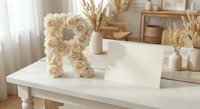 Decorative letter R made of cream roses on white table in bright modern interior with pampas grass and natural wooden furniture for home decor and styling.