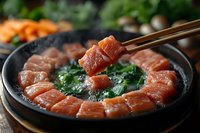 Fresh salmon sashimi arranged in stone bowl with spinach, chopsticks picking up a piece, blurred vegetables in background.
