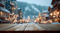 Wooden table overlooking snowy mountain village with illuminated Christmas trees and festive lights during evening snowfall.