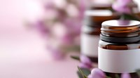 Cosmetic jars with blank labels on pink background with purple flowers, selective focus. Natural skincare and beauty product packaging mockup.