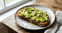 Avocado toast with herbs and olive oil on rustic bread served on white plate, healthy breakfast meal on wooden table by window for food photography.