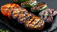 Grilled colorful vegetables with charred grill marks on black stone plate, seasoned with herbs and balsamic glaze. Fresh seasonal produce for healthy eating.