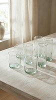 Set of clear green-tinted drinking glasses arranged on wooden table in bright natural light kitchen interior for home decor and dining concepts.