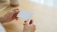 Hands holding blank white card on wooden desk with coffee cup, suitable for business branding, mockup design, and corporate identity presentations.