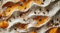 Rustic pumpkin pie surface with whipped cream swirls and scattered pumpkin seeds, showing rich autumn colors and textural details in macro photography.