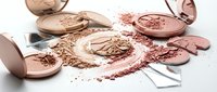 Broken rose gold makeup powder compacts scattered with crushed cosmetic powder and makeup brushes on white background for beauty product design.