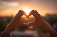Hands forming heart shape silhouette against warm sunset sky, romantic gesture expressing love and affection during golden hour outdoors.