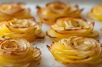 Delicate potato roses with crispy golden edges arranged in rows, baked to perfection with subtle seasoning, showcasing innovative food presentation for restaurants.