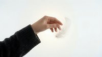 Hand in dark knit sweater gently holding a white feather against a bright white background, symbolizing lightness, delicacy, and softness.