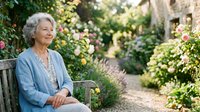 Senior woman with gray hair sitting on wooden bench in lush garden surrounded by blooming flowers and climbing vines, relaxing outdoors in natural setting.